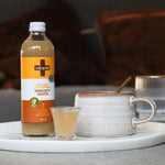 Bottle of Daily Good Ginger immunity shots alongside cup of tea 